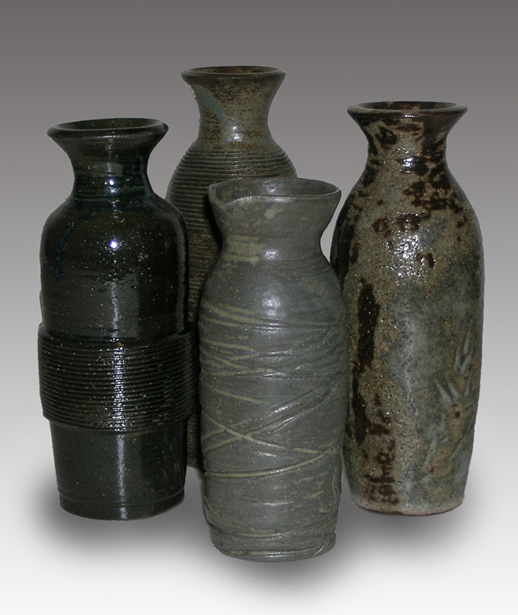 Four tall clay pots with different carved designs around the sides. Two are gray, one is gray and black and the fourth is all black